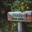 Sign in wooded area with word TRAIL and left-pointing arrow